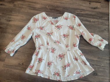 Pembe çiçeklerin güzel bir dizaynını içeren beyaz bir gömlek, sıcacık bir ahşap zeminde dinleniyor ve uzaya cazibe katıyor.