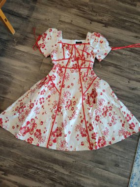 Canlı kırmızı çiçeklerle süslenmiş güzel beyaz bir elbise kırsal bir ahşap zeminde zarif bir şekilde yatıyor ve güzel bir görsel karşıtlık oluşturuyor.