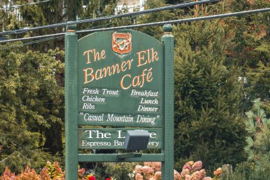 Çam ormanlarının girişinin yanındaki el boyaması tabela, çiçek ve ormanla kaplı rahat dağ pankartı.