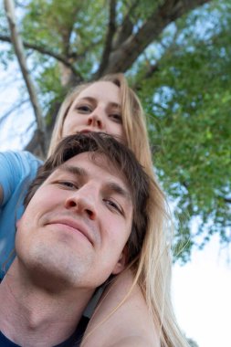 Bir erkek ve bir kadın büyük, güzel, yeşil bir ağacın önünde birlikte poz veriyorlar.