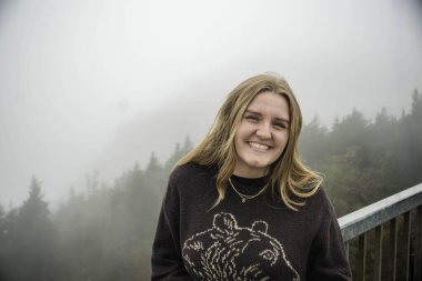 Bir kadın zarif bir şekilde parmaklıklarda oturuyor, etrafını kalın bir sis kaplıyor ve etrafını gizem ve güzellikle donatıyor.