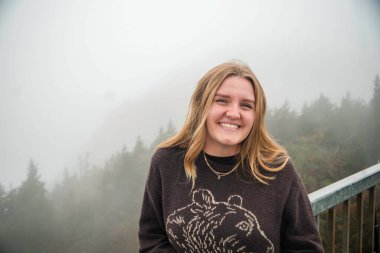 Sevimli bir ayı tasarımı içeren rahat bir süveter giymiş bir kadın zarif bir şekilde güzel bir köprüde duruyor.