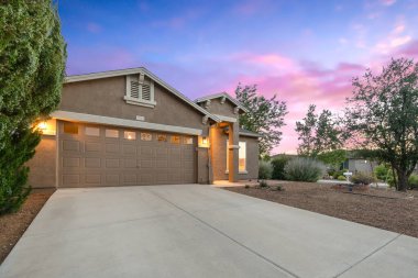 Bir garaj yolunun yanında ferah bir garaj barındıran güzel bir ev. Gün batımının resimli arka planına karşı kurulmuş.