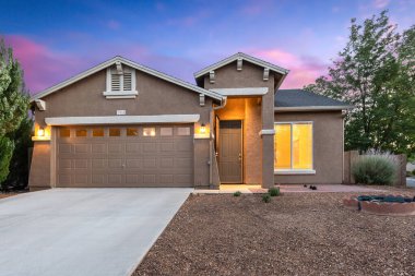 Geniş bir garaj ve davetkar bir garaj içeren büyüleyici bir ev geceleri güzelce aydınlatılıyor ve güzel bir manzara yaratıyor.