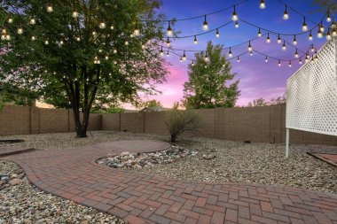 Büyüleyici bir tuğla geçidi olan güzel bir bahçe, yukarıdaki tavandan nazikçe sarkıtılmış sicim ışıklarıyla tamamlanmış.