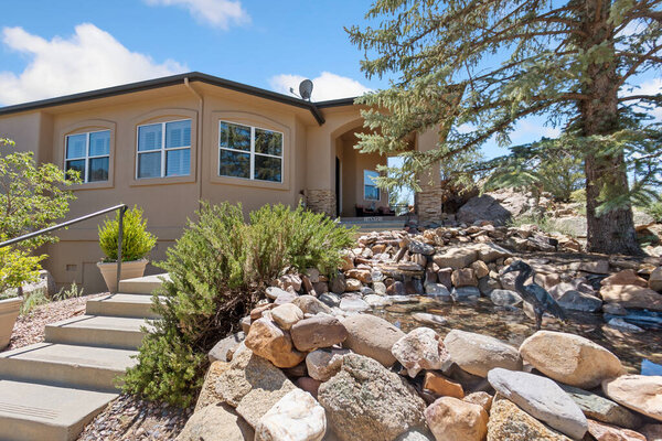 This charming house, which features a lovely set of stairs leading up to its entrance, is beautifully surrounded by various rocks and tall trees