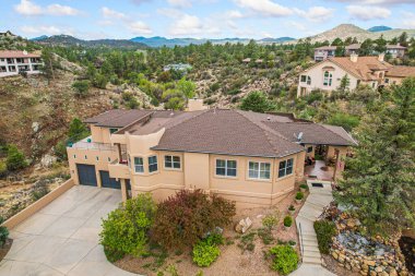 Etkileyici bir hava manzarası, manzaralı bir tepenin üzerinde büyük, görkemli bir ev yakalıyor. Arka planda büyüleyici dağlar yükseliyor.