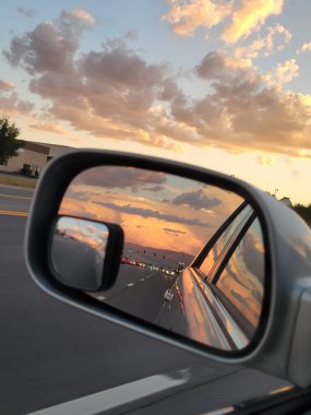 Çarpıcı bir gün batımı, bir arabanın yan aynasına güzelce yansıyarak hayranlık uyandıracak güzel ve büyüleyici bir sahne yaratır.