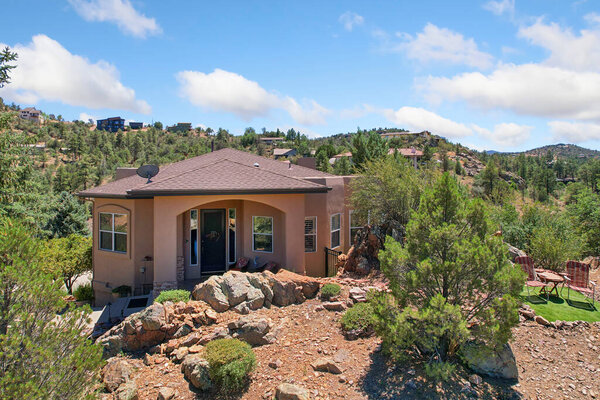 A spacious large house is elegantly positioned atop a picturesque hill, beautifully surrounded by lush trees and scattered rocks in the landscape