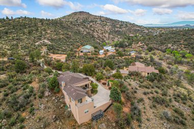 Geniş bir hava manzarası, verimli ağaçlar ve canlı bitkilerle çevrili bir tepenin üzerinde zarif bir şekilde tünemiş resimli bir ev yakalar.