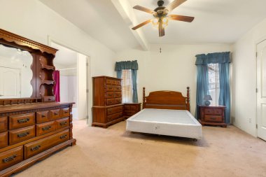 Yatak odasında rahat bir yatak, şık bir şifonyer, uzun bir ayna ve rahatlamak için ferahlatıcı bir tavan vantilatörü var.