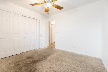 Üzerinde tavan vantilatörü olan boş bir yatak odası ve bir duvar boyunca giysi ve eşyalar için geniş bir depo sağlayan geniş bir dolap.