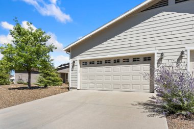 Geniş bir garaj kapısı ve eve kolay erişimi olan hoş bir beyaz ev.