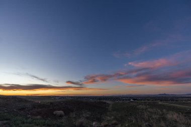 Yumuşak, pembe bulutlarla bezenmiş canlı bir mavi gökyüzünü gösteren, büyük, resimsi bir tarlanın üzerinde güzel bir gün batımı.