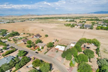 Sersemletici hava manzarası geniş kuru topraklar ve açık mavi gökyüzü arasında banliyö evleri gösteriyor..