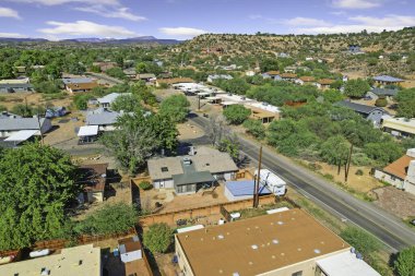 Çatıları olan ana cadde görünür ticaret, park edilmiş araçlar, elektrik direkleri, ağaç tepe örtüsü.,