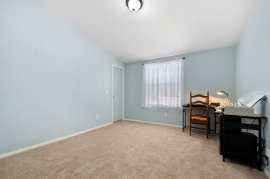 İçinde minimalist bir atmosfer yaratan, içinde bir sandalye bulunan, basit bir masa olan boş bir yatak odası var.