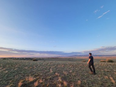 Yalnız bir adam uçsuz bucaksız bir tarlanın ortasında dikiliyor, dikkatle gökyüzüne bakıyor.