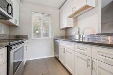 Beyaz dolaplar, modern paslanmaz çelik aletler, lavabo ve doğal ışık sağlayan büyüleyici bir pencere içeren güzel tasarlanmış bir mutfak.