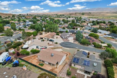 Sersemletici hava manzarası banliyö mahallesini gösteriyor, güneş panelleri olan evler, yemyeşil alanlar ve mavi gökyüzünün altında sakin bir manzara..