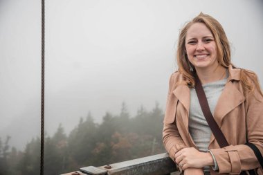 Bir kadın zarif bir şekilde parmaklıklarda oturuyor, etrafını kalın bir sis kaplıyor ve etrafını gizem ve güzellikle donatıyor.