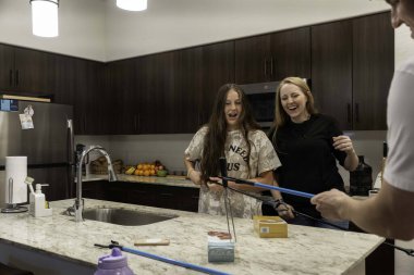 İki arkadaş keyifli bir aktiviteyle meşgul olurken şık bir mutfakta neşeli bir anı paylaşıyorlar. Sahne, modern ortamda kahkaha ve dostluğu yakalıyor..