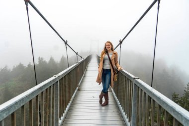 Şehir sisinin ortasında kendinden emin bir kadın gezgin, sise karşı ihtiyatlı bir güvenle köprüde sarışın bir kadın.