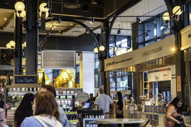 Bir grup birey, çeşitli tasarım elementleriyle çevrili canlı bir restoran ortamında ayakta duruyor ve sohbet ediyorlar.