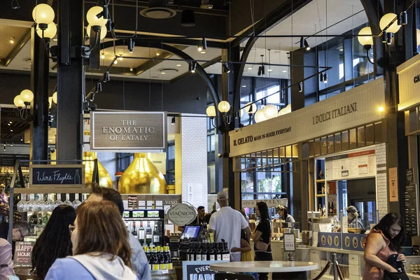 Bir grup birey, çeşitli tasarım elementleriyle çevrili canlı bir restoran ortamında ayakta duruyor ve sohbet ediyorlar.