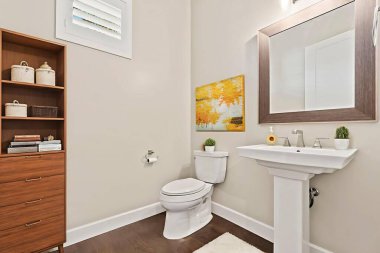 Yaya lavabosu, tahta rafı, çerçeveli aynası, tuvaleti ve dekoratif sanatı olan misafir banyosu.