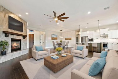 Şömineli rahat bir oturma odası, dokuma sehpası etrafında pelüş koltuklar, tavan vantilatörü, raflarda inşa edilmiş.,