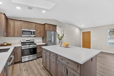 Geniş adalı, ahşap dolaplı, paslanmaz aletli, kuvars tezgahlı parlak modern mutfak.