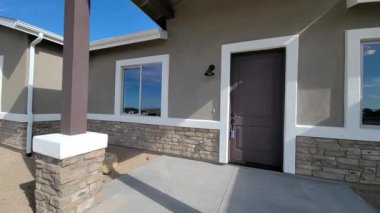 Taş sütunlu büyüleyici giriş, boyanmış kapı ve veranda betonu, güneş ışığı gölgeleri.