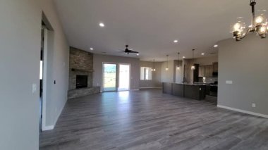 Şömineli bir aile odası, arka bahçeye açılan kapılar, geniş döşemeli döşemeler ve avize ışıklandırması.