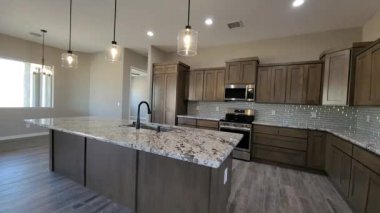 Ada, granit tezgah, ahşap dolaplar ve kolye ışıkları olan geniş çaplı aşçı mutfağı.