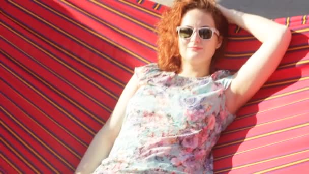 年轻红卷曲头发的女人正躺在一张吊床上，放松下太阳慢动作. — 图库视频影像