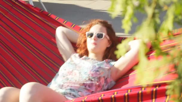 Red Curly Hair Girl está deitada em uma rede, relaxando sob o sol. Movimento lento . — Vídeo de Stock