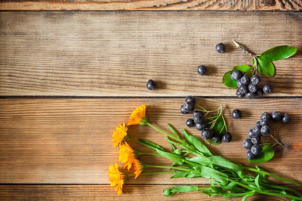 Άνθη καλέντουλας και οι καρποί της αρώνιας (μαύρο chokeberry) σε ξύλινο υπόβαθρο σε ρουστίκ στυλ — Φωτογραφία Αρχείου