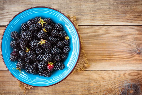 Fresh blackberries in blue ceramic bowl on wooden background in rustic style — Stock Photo, Image