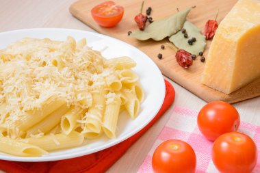 Penne makarna bir beyaz üstüne rendelenmiş peynir ile yuvarlak tabak baharatlar ve domates masada yanında