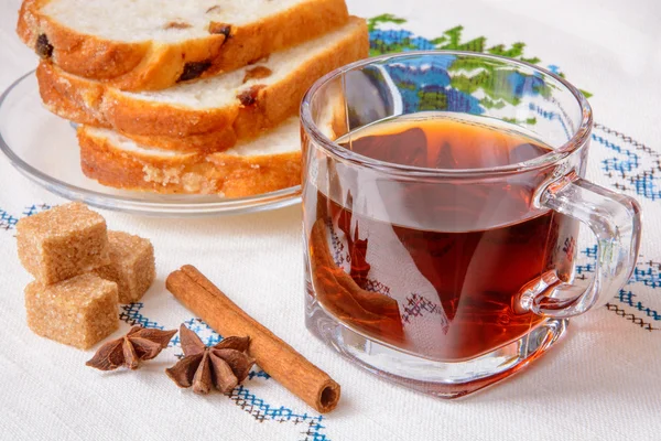 Чашка чая с коричневым сахаром, анисом, корицей и хлебом на скатерти — стоковое фото