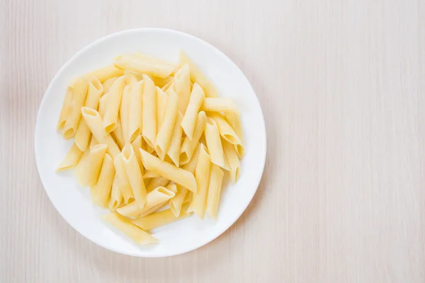 Ahşap arka plan üzerinde beyaz yuvarlak tabakta Penne makarna — Stok fotoğraf