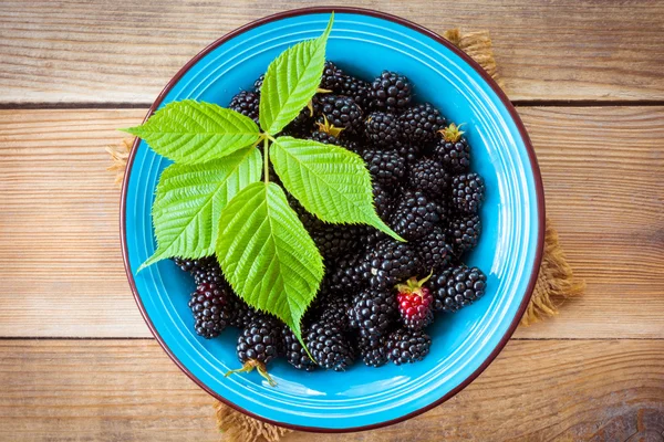 Frische Brombeeren mit Blättern in blauer Keramikschale auf Holzgrund im rustikalen Stil — Stockfoto