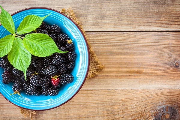 Fresh blackberries with leaves in blue ceramic bowl on wooden background in rustic style — Stock Photo, Image