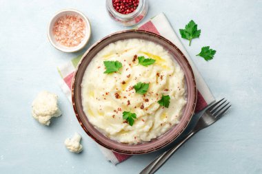 Tereyağlı karnabahar ezmesi, pembe biberler ve beton arka planda maydanoz. Üst görünüm.