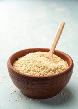 Beyaz susam tohumları seramik kasede, tahta kaşıkla beton arka planda. Seçici odak.