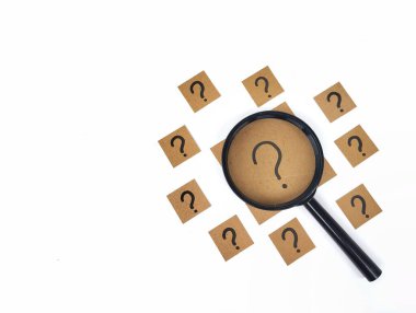 Kahverengi kağıda yazılmış soru işareti el yazısı ve beyaz arka planda büyüteç.