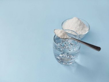 Salt water solution in glass and pile of salt with spoon on blue background. Copy space 