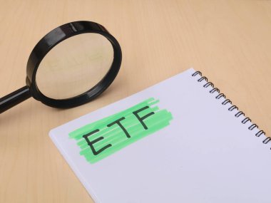 ETF kısaltması deftere yatırım araştırma konsepti için büyüteçle el yazısıyla yazılmış. Finansal analizi, piyasa araştırmasını ve borsa yatırım stratejilerini sembolize eder