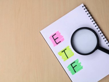 ETF kısaltmasının en üst görüntüsü deftere yatırım araştırma konsepti için büyüteçle birlikte el yazısıyla yazılmış. Finansal analizi, piyasa araştırmasını ve borsa yatırım stratejilerini sembolize eder